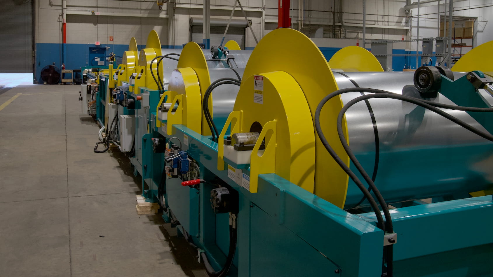 Industrial production line with large yellow spool rollers mounted on a teal frame inside a factory.