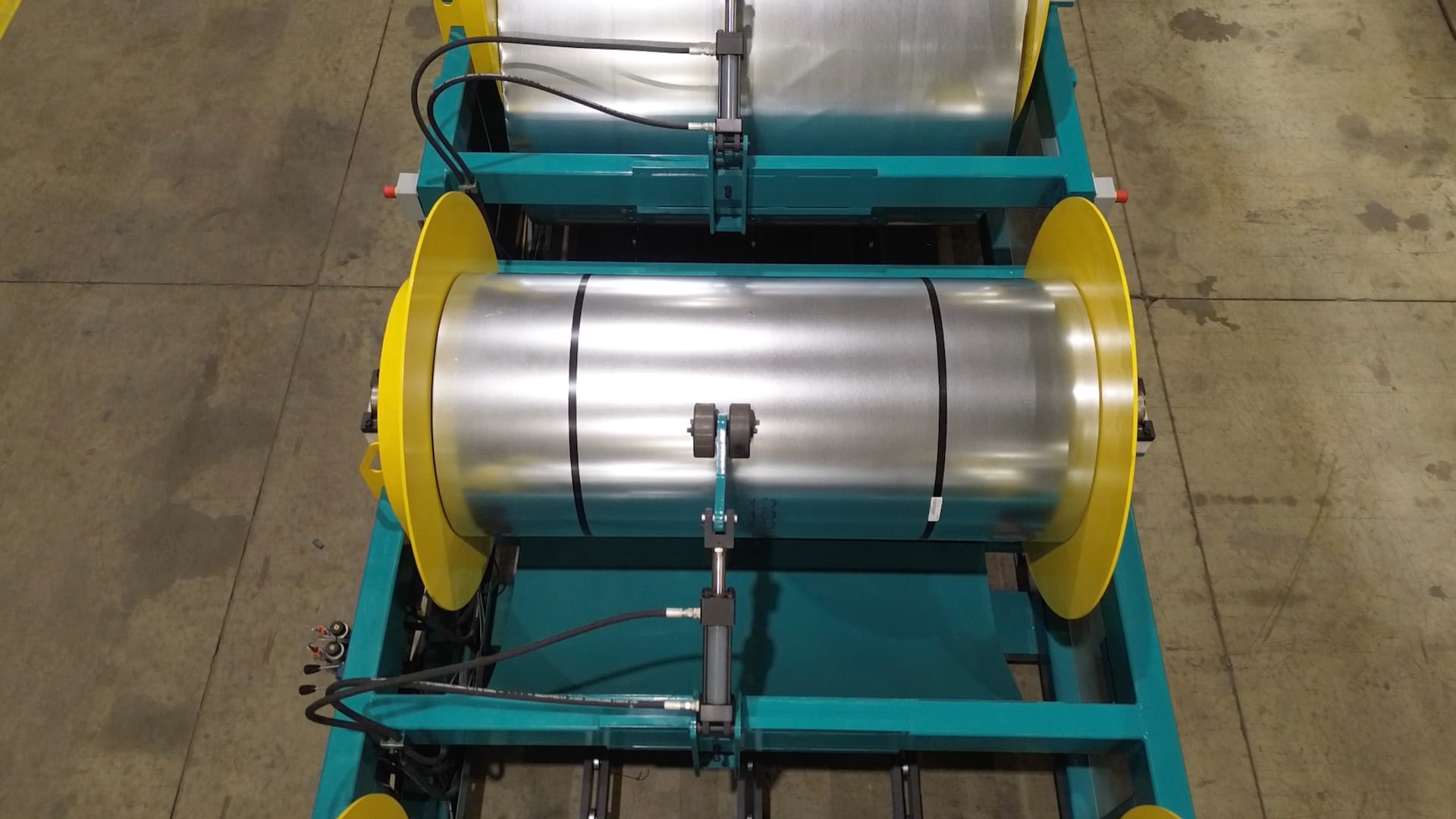 Industrial roller machine with two large chrome rollers on a teal frame and bright yellow end disks