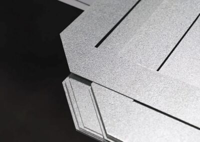 Close-up of a gray textured geometric metal panel with sharp angles and dark seams against a black background.