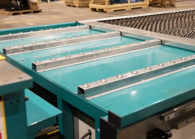 Teal industrial conveyor system with riveted silver guide rails in a warehouse setting.