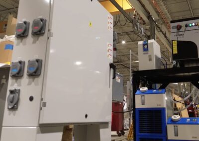 Industrial factory scene with large gray electrical cabinets, control switches, and blue cooling units on a metal frame.