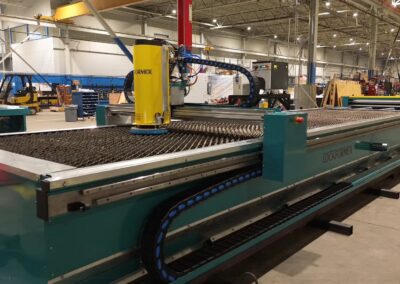 Industrial factory floor with a large teal sheet-metal cutting machine and a yellow robotic arm in the foreground